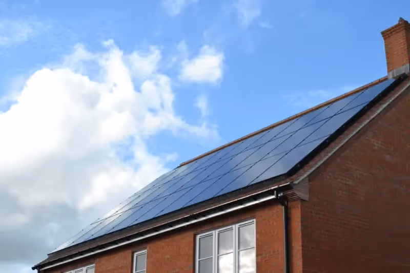 Picture of solar panels on a roof, looking up from the ground with blue sky and a small amount of cloud in background