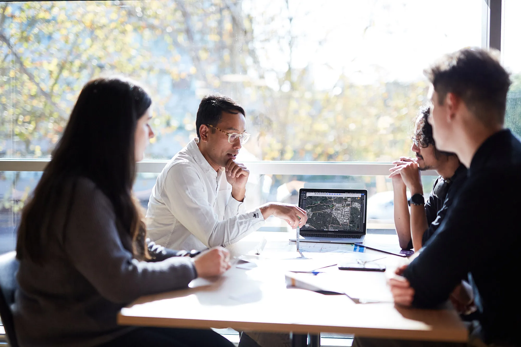 Four people having a discussion around a table with a laptop displaying a map.