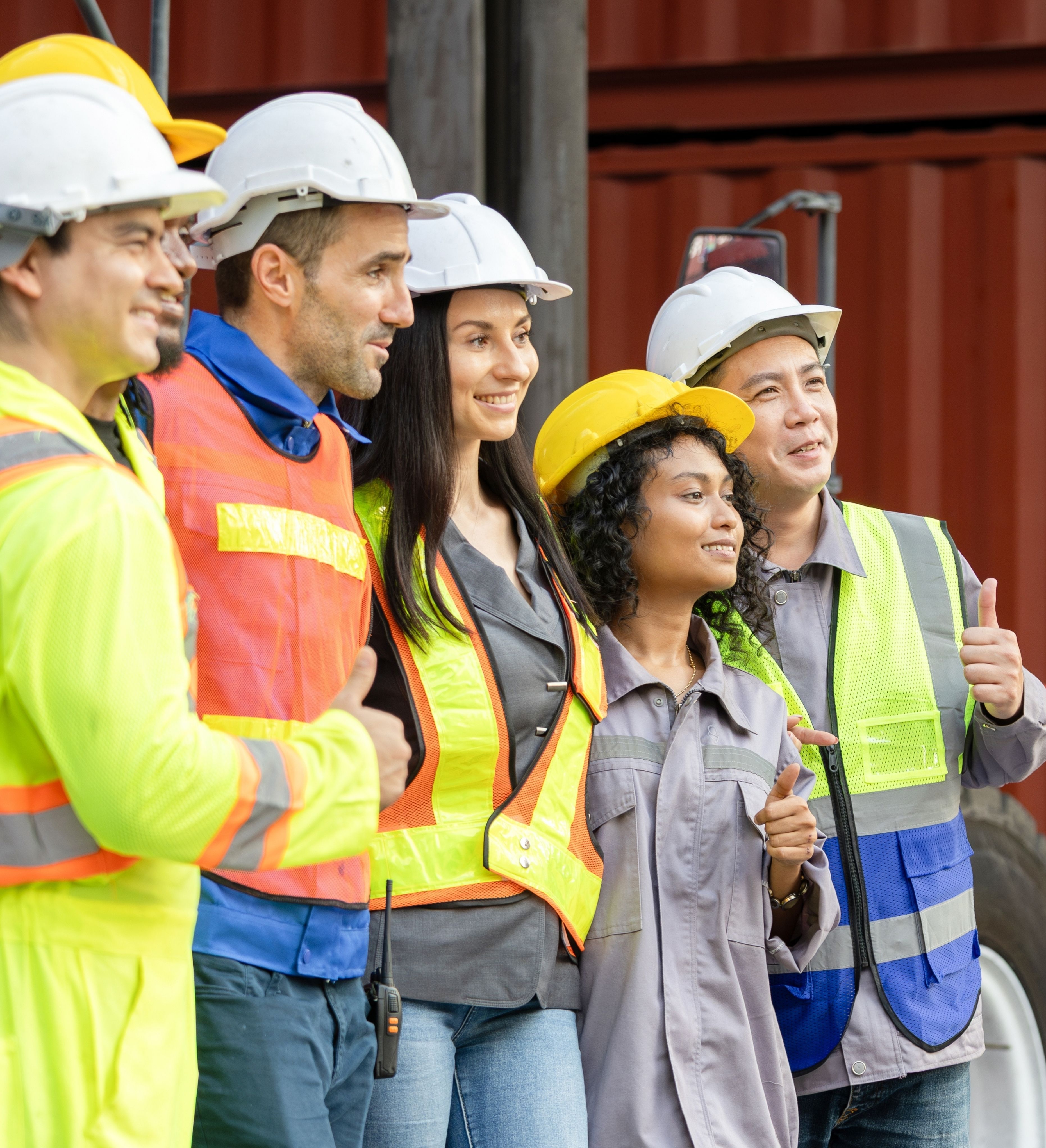 Group of diverse construction workers wearing safety helmets and vests giving thumbs up.