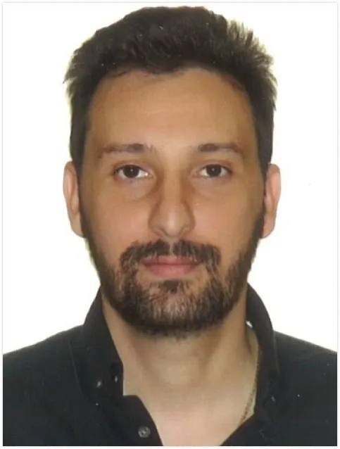 Portrait d'un homme avec une barbe courte et des cheveux foncés, portant une chemise noire.