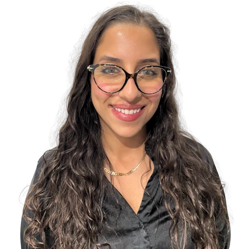 Jeune femme souriante portant des lunettes à monture noire et une chemise noire, avec de longs cheveux bouclés bruns.