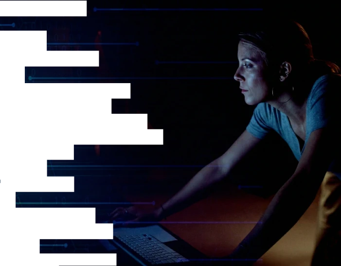 Femme concentrée travaillant sur un ordinateur dans une pièce sombre, avec des éléments graphiques bleus transparents autour.