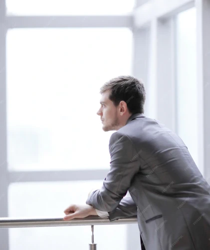 Homme d'affaires regardant pensivement par une fenêtre dans un bureau lumineux.