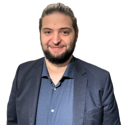 Jeune homme souriant avec barbe, chemise bleue à motifs et veste bleu marine.