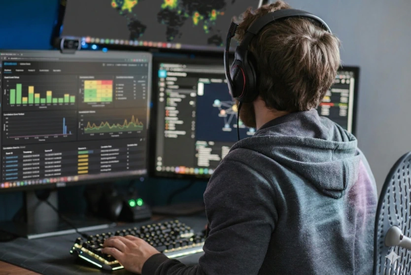 Homme portant un casque, assis devant deux écrans d'ordinateur affichant des graphiques et des données analytiques.