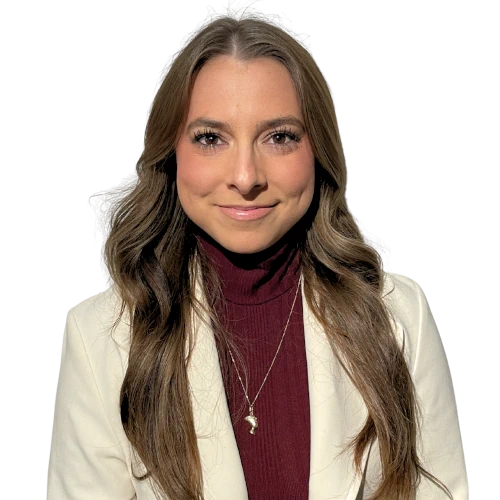 Portrait d'une femme souriante aux longs cheveux bruns ondulés, vêtue d'un pull col roulé bordeaux et d'une veste blanche, avec un collier argenté.