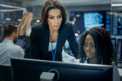 Deux analystes en cybersécurité concentrées devant un écran d'ordinateur dans un bureau moderne.