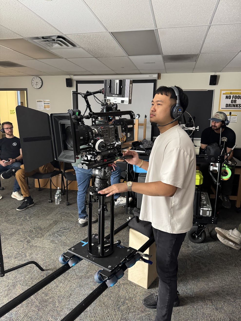 Man operating professional video camera on a dolly rig, wearing headset in an indoor studio setting.