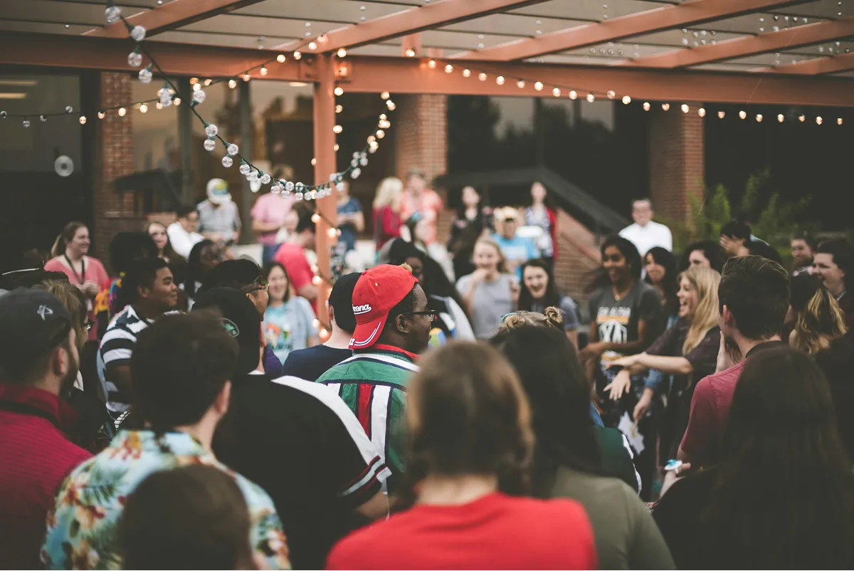 Group of people socializing under string lights at an outdoor event.