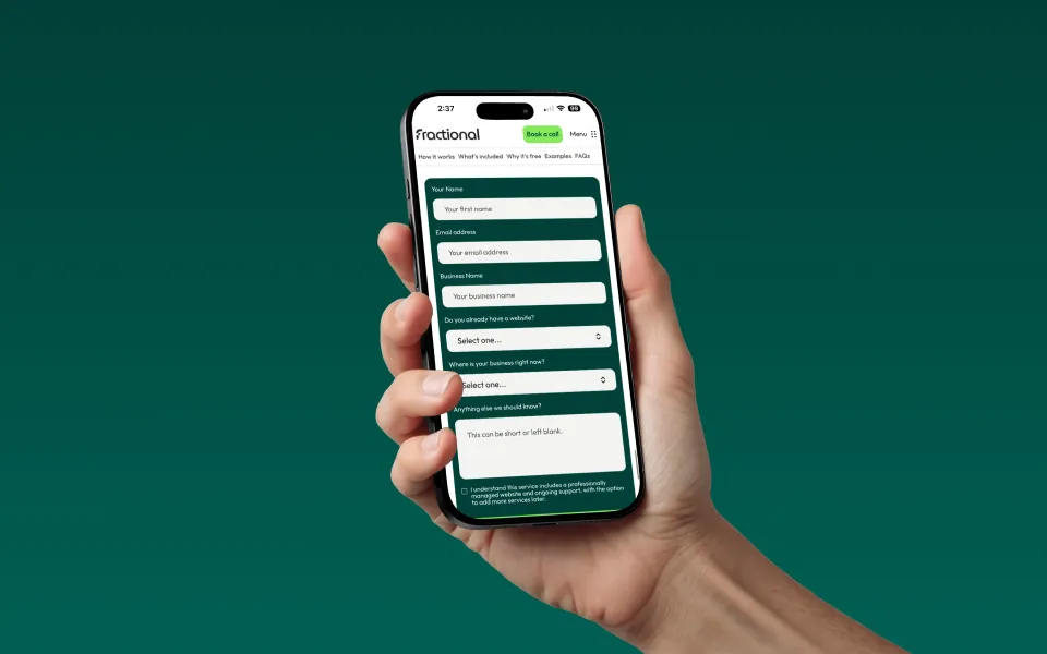 Hand holding a smartphone displaying a website form on 'fractional' with fields for name, email, business name, website status, business location, and additional notes.