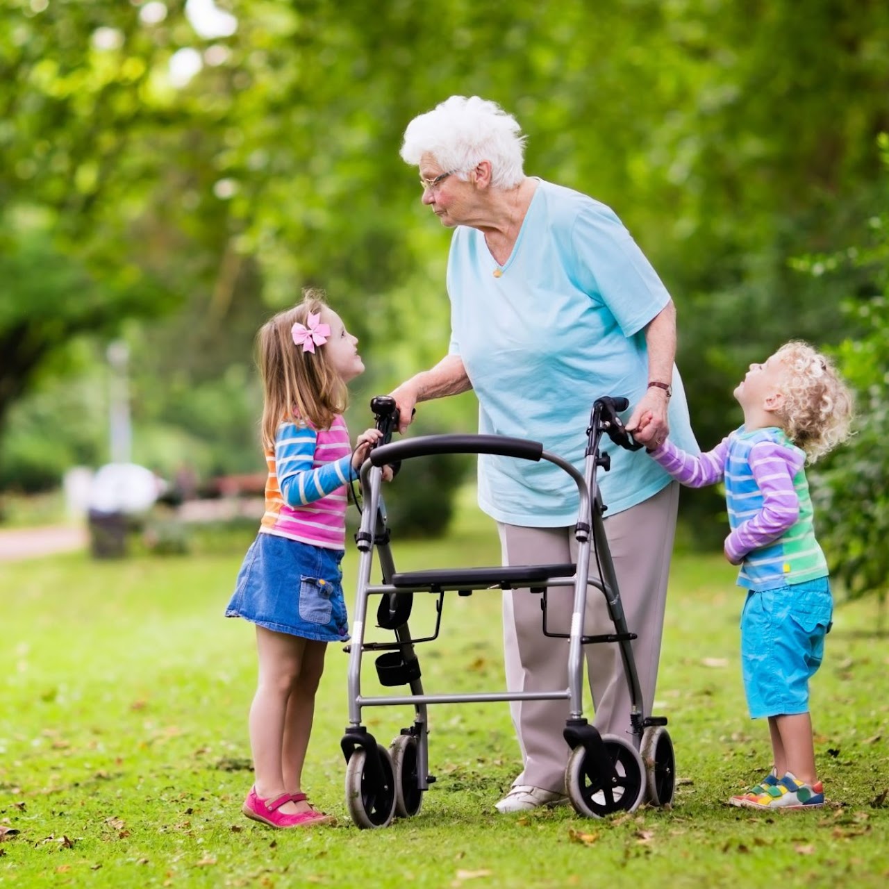 Elderly woman with white hair using a walker outdoors, interacting warmly with two young children.