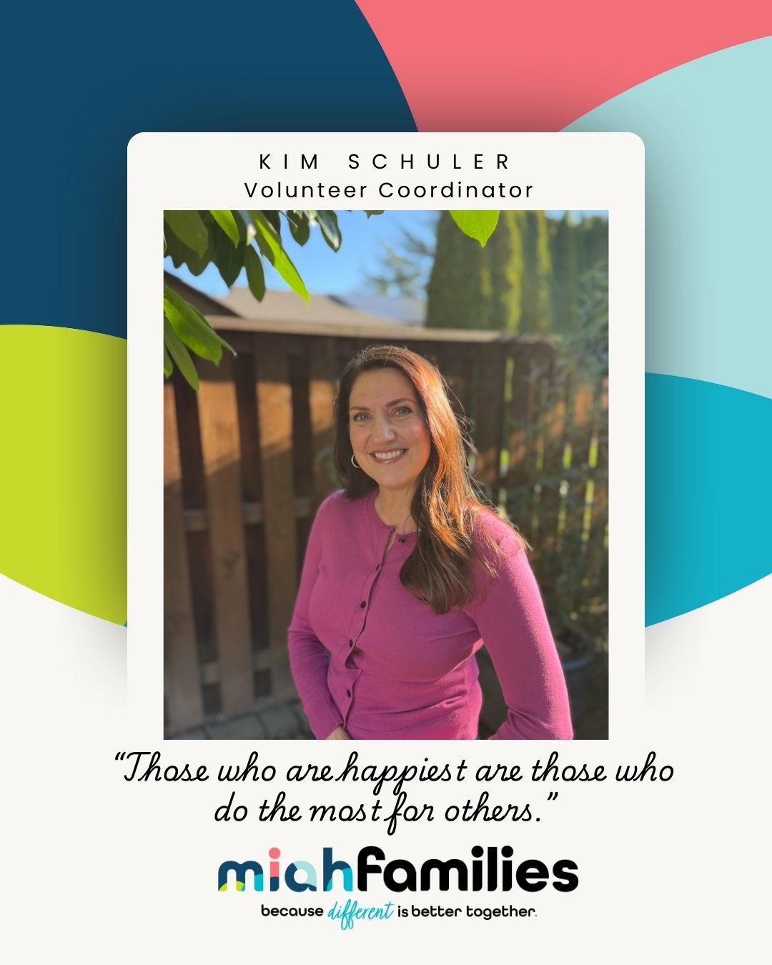 Portrait of Kim Schuler, Volunteer Coordinator, smiling outdoors wearing a pink cardigan with a wooden fence and greenery in the background.