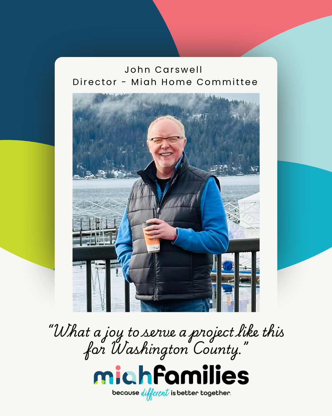 John Carswell, director of Miah Home Committee, smiling and holding a coffee cup by a lakeside with forested hills in the background.