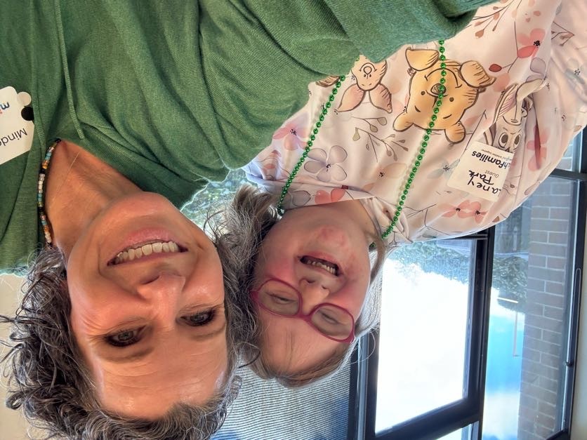 Two smiling women taking a selfie indoors, one wearing a Winnie the Pooh hoodie and glasses.