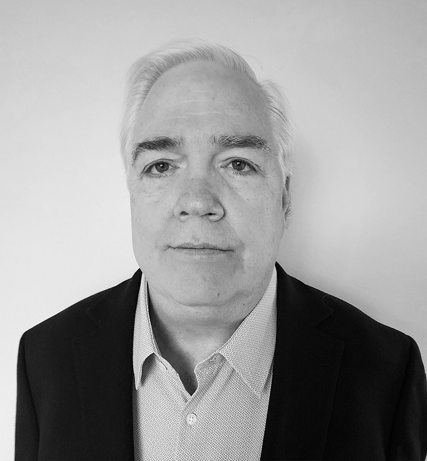 Black and white headshot of Kevin Feeley wearing a dark blazer and patterned dress shirt against a plain background.