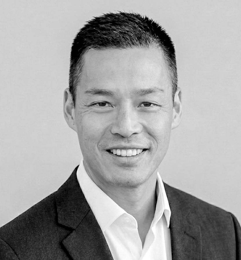 Ken-ichi  Hino wearing a dark suit jacket and white dress shirt against a plain background.