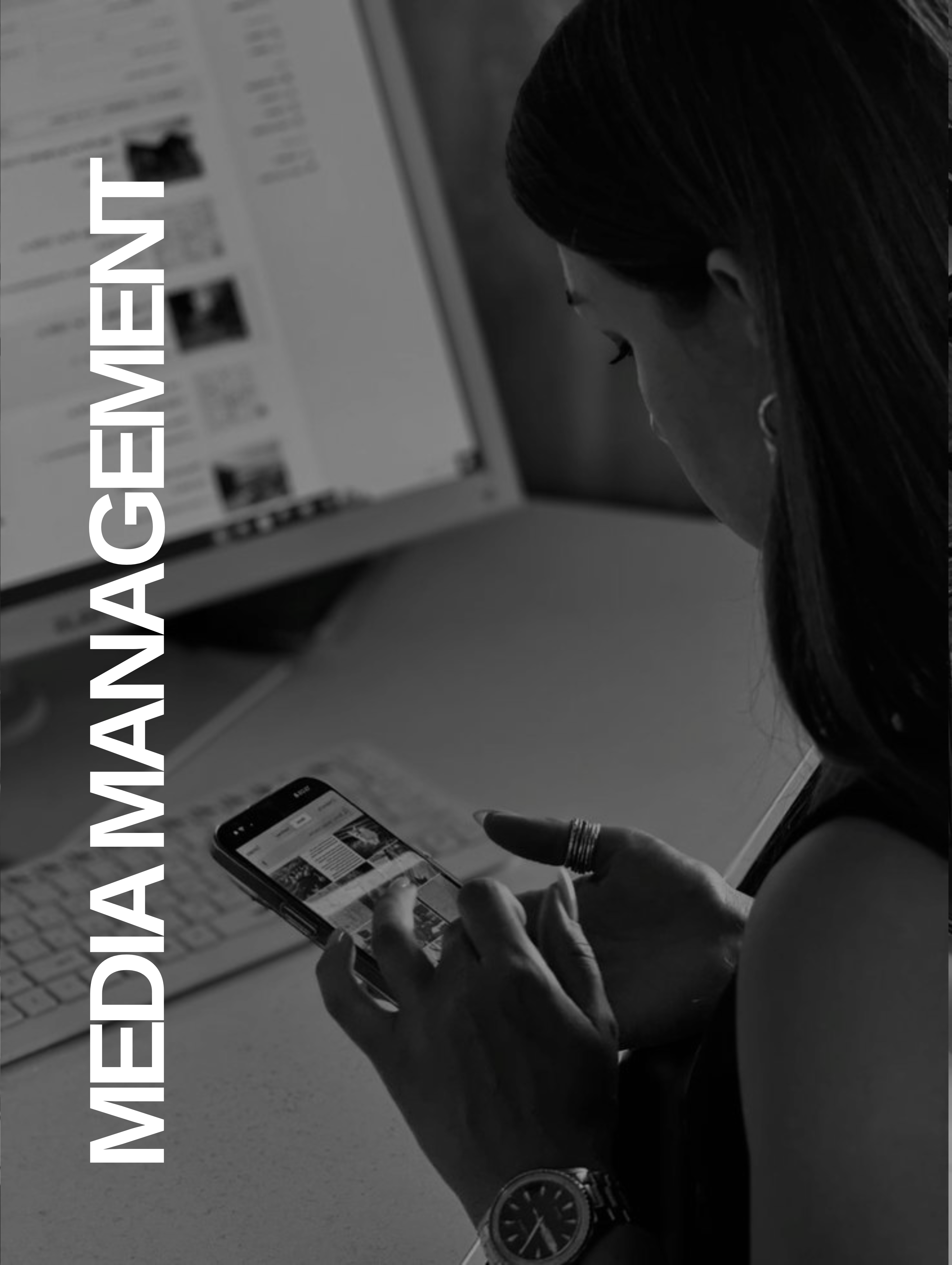 Woman browsing social media on smartphone with computer screen and keyboard in the background.