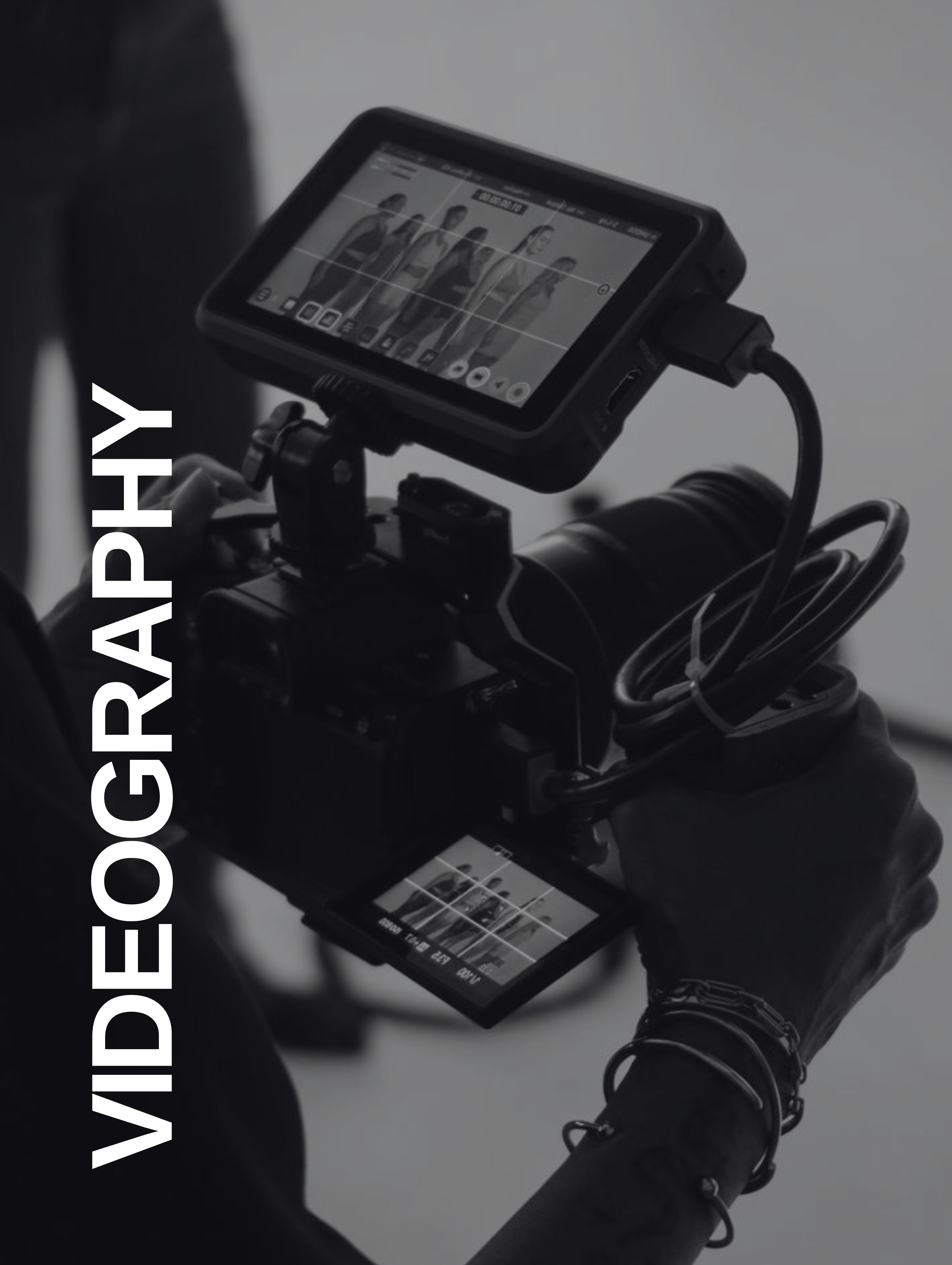 Person holding a professional video camera showing women models on two small display screens.