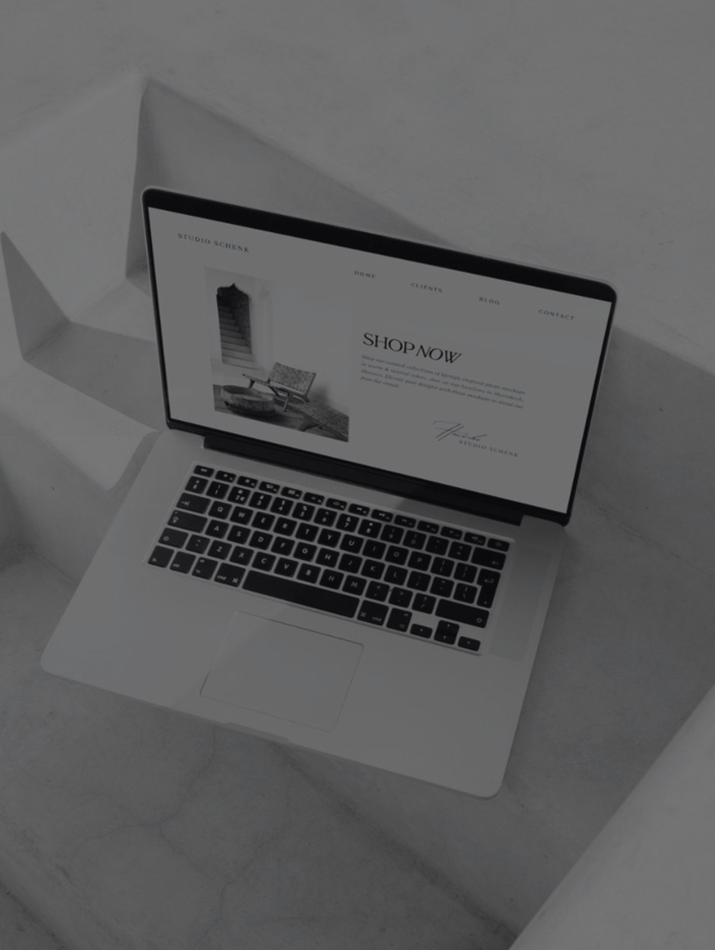 Open laptop on concrete steps displaying a minimalist website with a Shop Now section and navigation links.