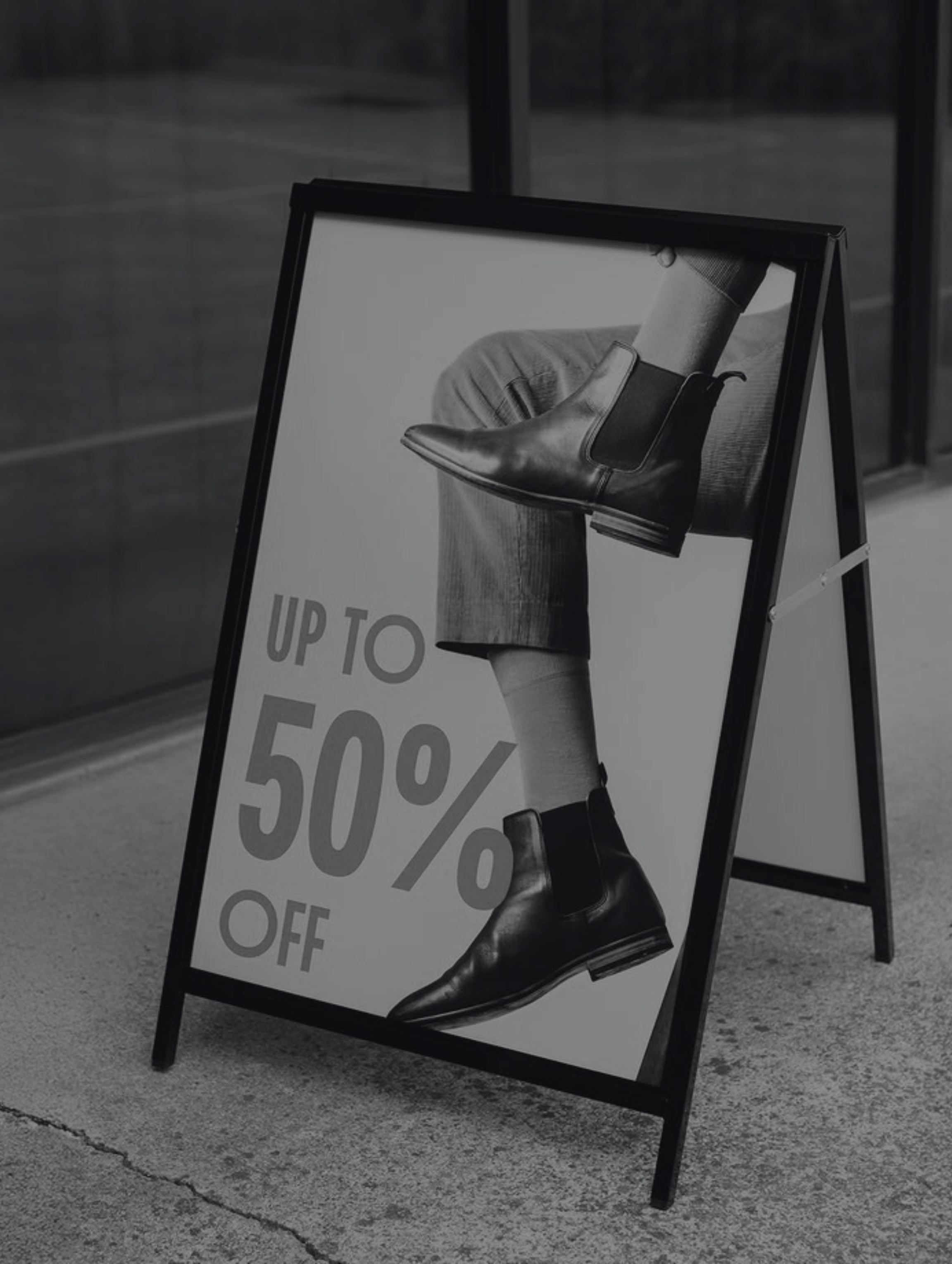 Sidewalk sign advertising up to 50% off with image of a person wearing black leather boots.