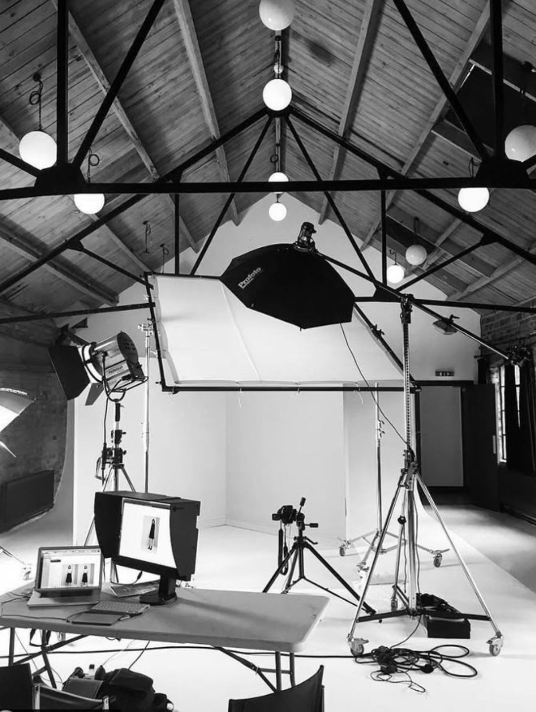 Indoor photography studio with lighting equipment, tripods, and monitors on a table.