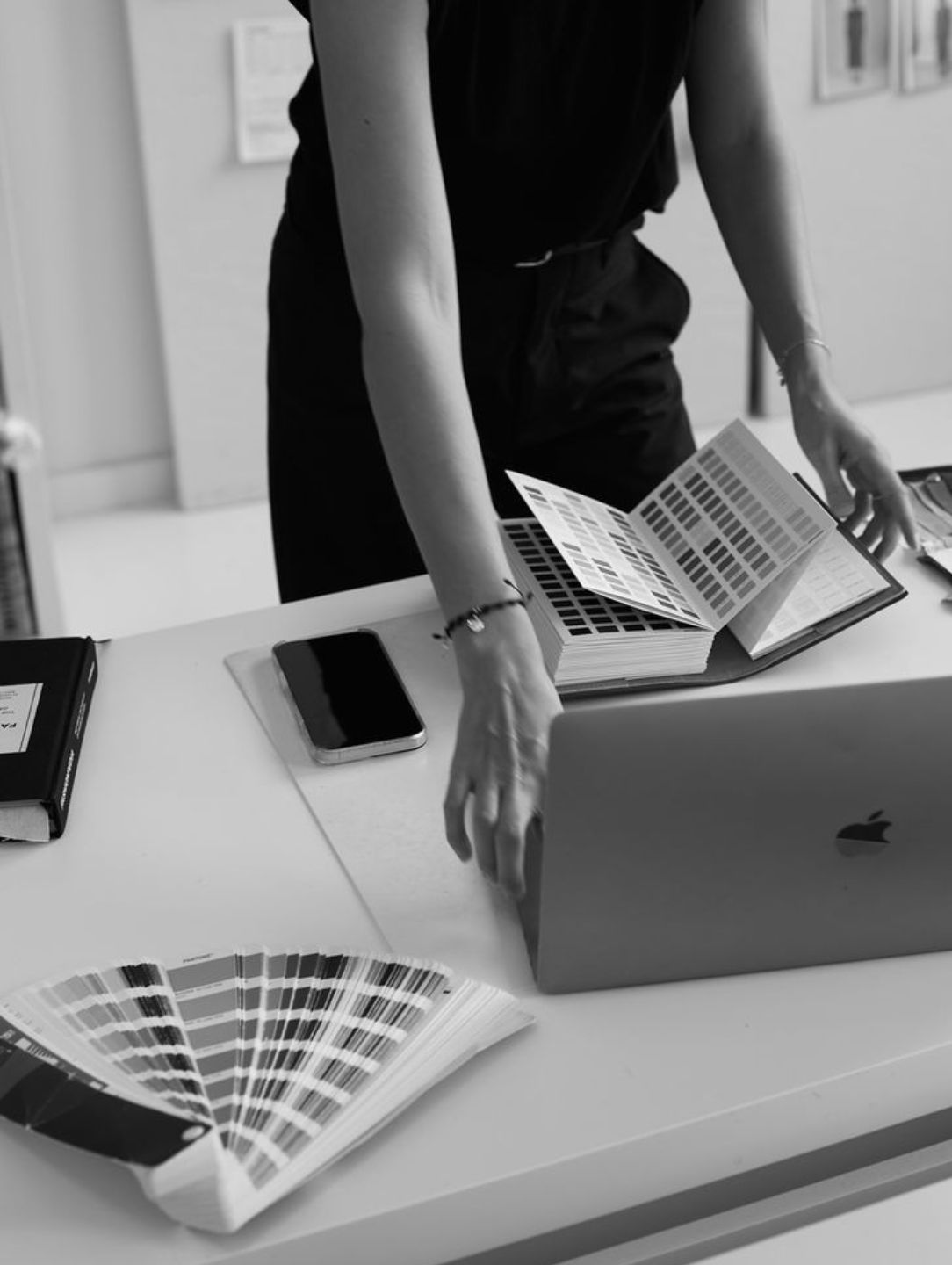 Person working at a desk with a color swatch book, laptop, and smartphone.