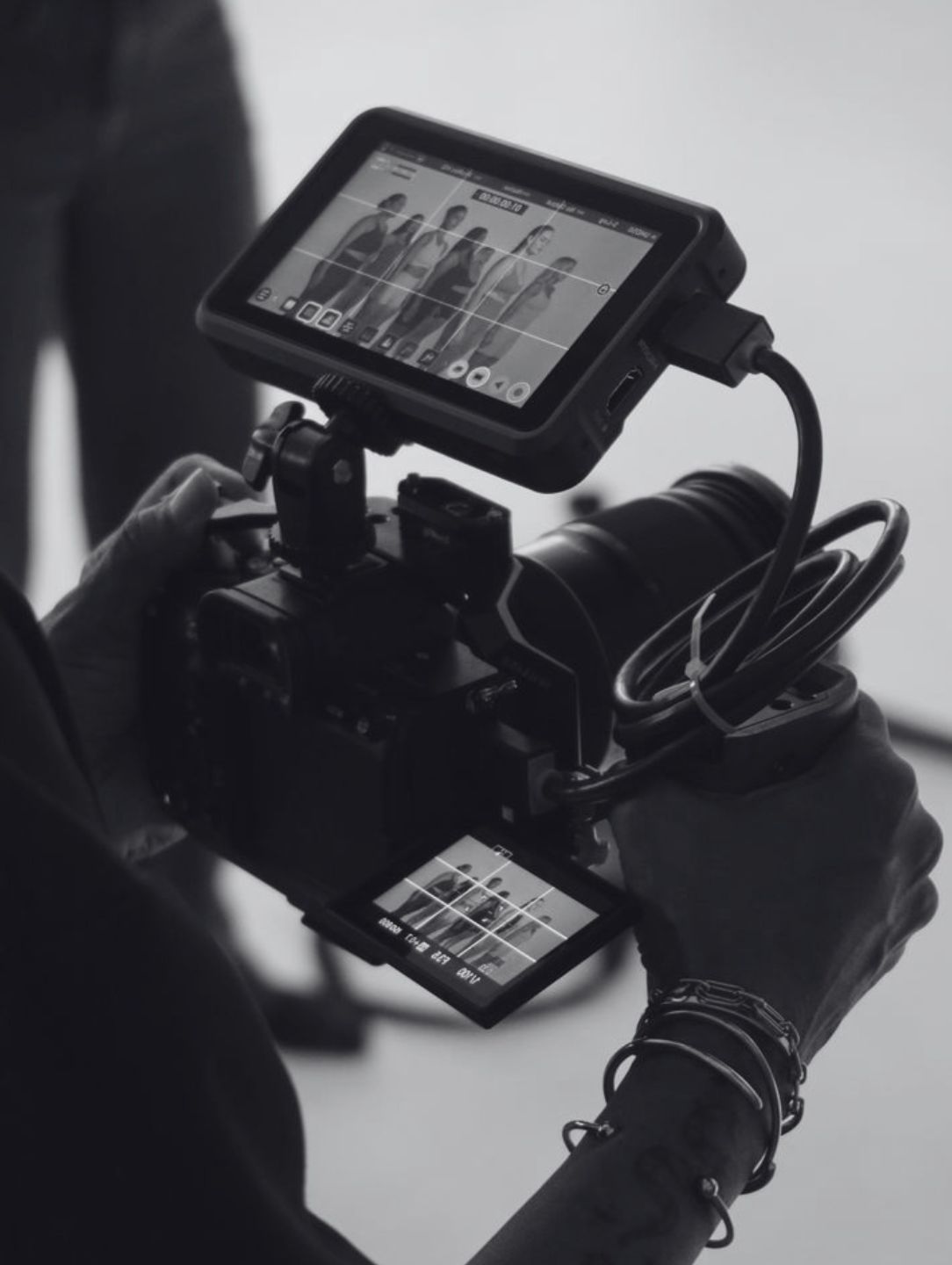 Hands holding a professional camera with external monitor showing a group of models posing.