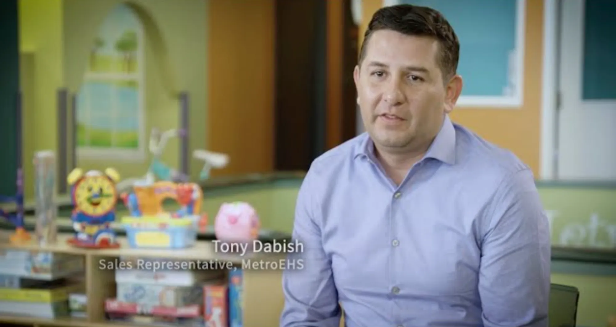 Man in a light blue shirt identified as Tony Dabish, Sales Representative at MetroEHS, seated in a colorful room with children's toys.