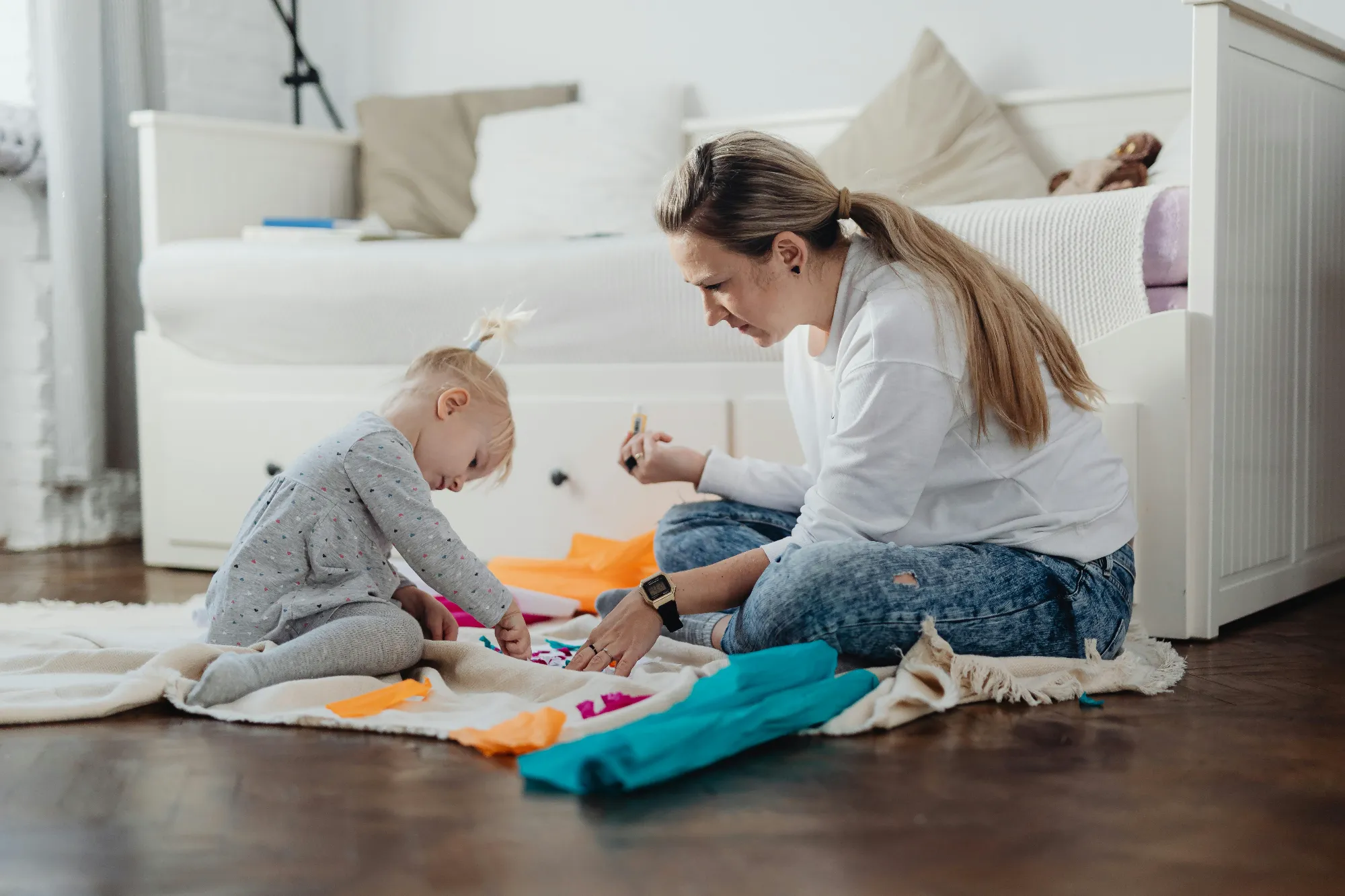 Woman and young girl sitting on the floor playing with colorful paper crafts in a cozy bedroom.