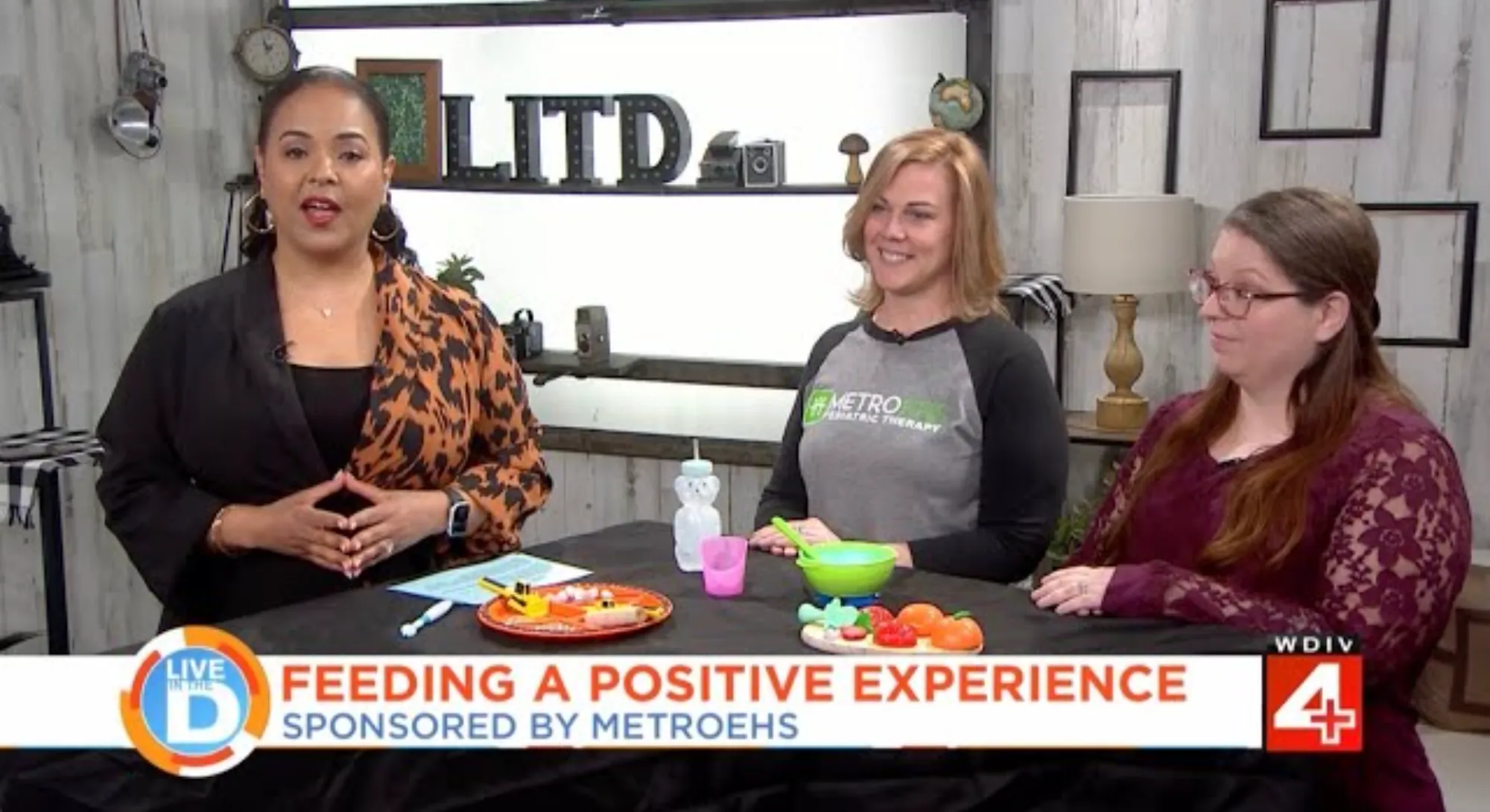 Three women sitting at a table with toy food and utensils, discussing feeding positive experiences on a Live In The D segment.
