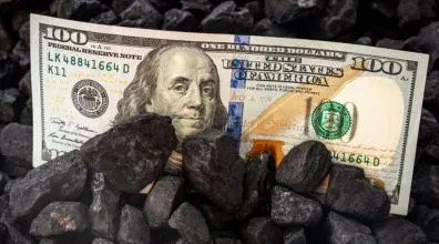 A US $100 bill featuring Benjamin Franklin partially buried in a pile of black coal lumps.