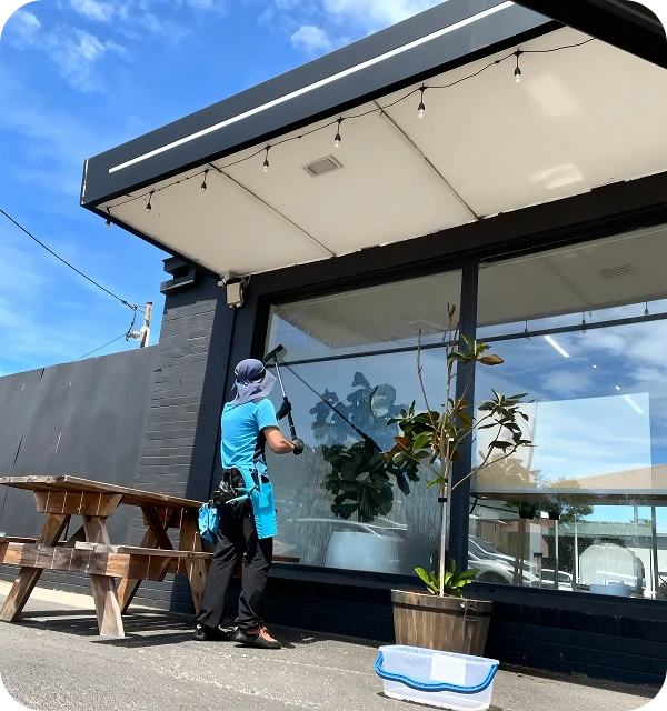 A woman is cleaning the windows of a restaurant, ensuring a clear view for customers outside