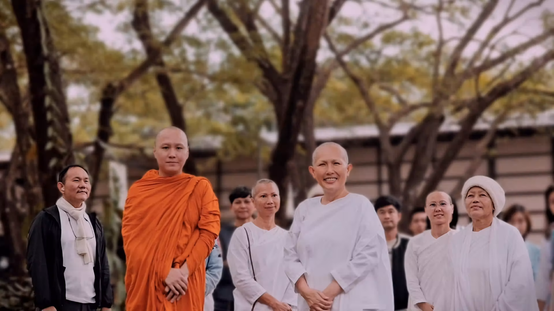 A group of Buddhist monks and nuns standing outdoors under trees with peaceful expressions.