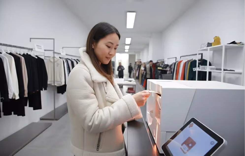 Woman in light-colored jacket scanning a card at a self-checkout machine in a modern clothing store.