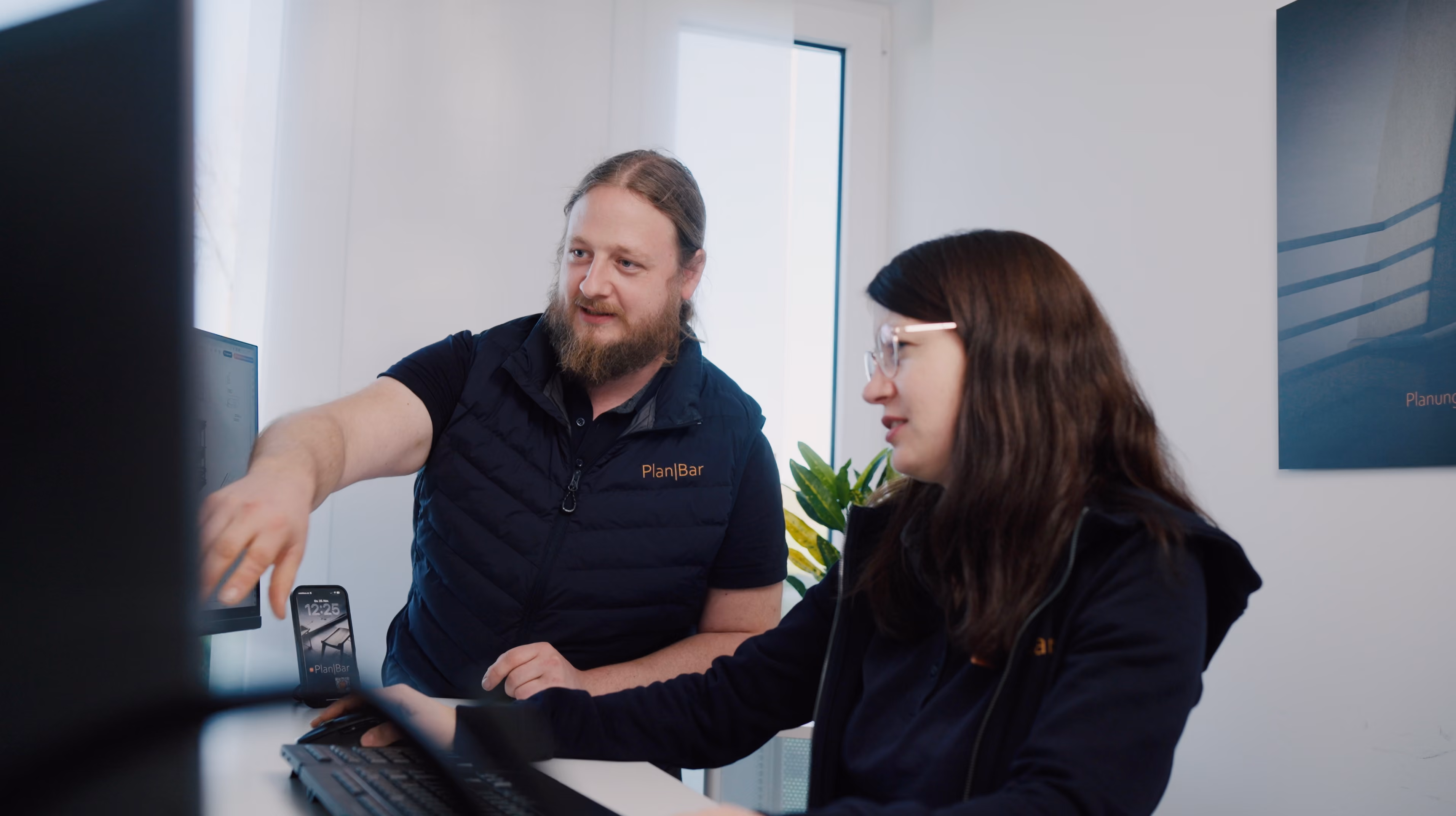 Twee medewerkers staan voor de computer en bespreken een project.