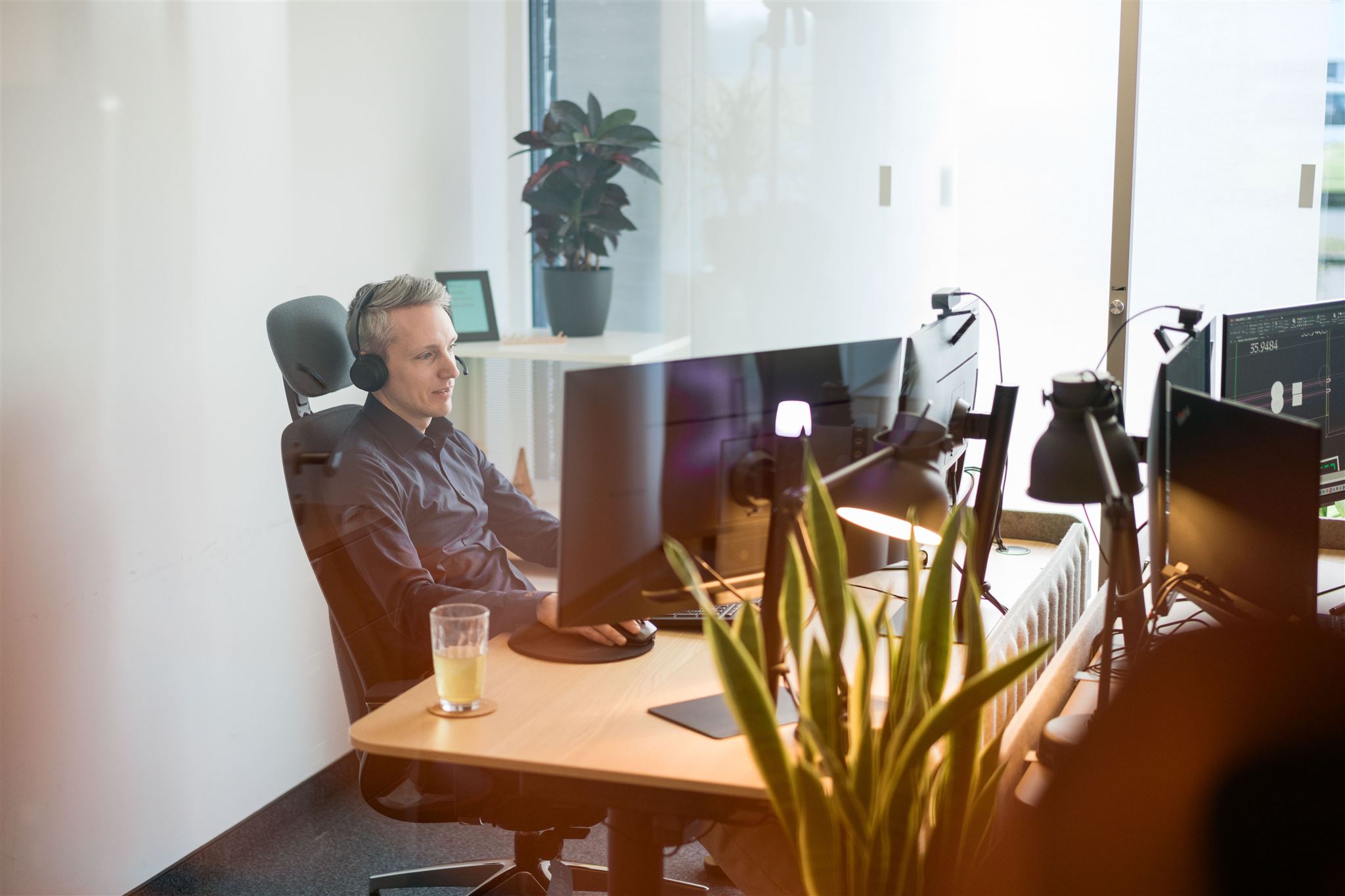 Mann mit Kopfhörer arbeitet am Schreibtisch mit mehreren Monitoren in einem hellen, modernen Büro.
