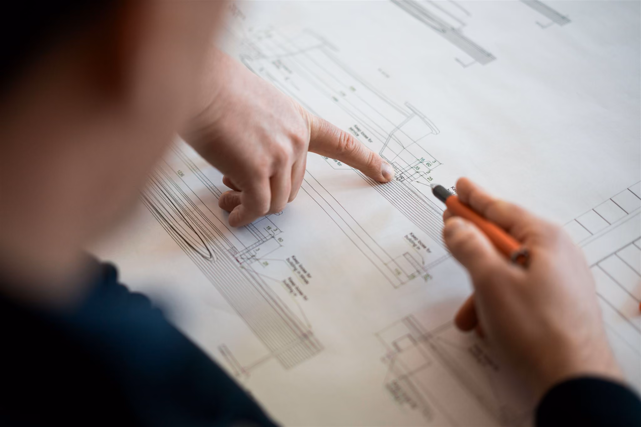 Eine Person zeigt mit dem Finger auf einen technischen Plan und hält einen Stift in der anderen Hand.