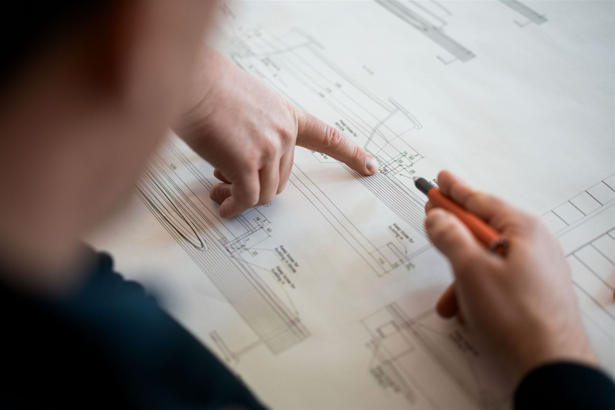 Eine Person zeigt mit dem Finger auf einen technischen Plan und hält einen Stift in der anderen Hand.