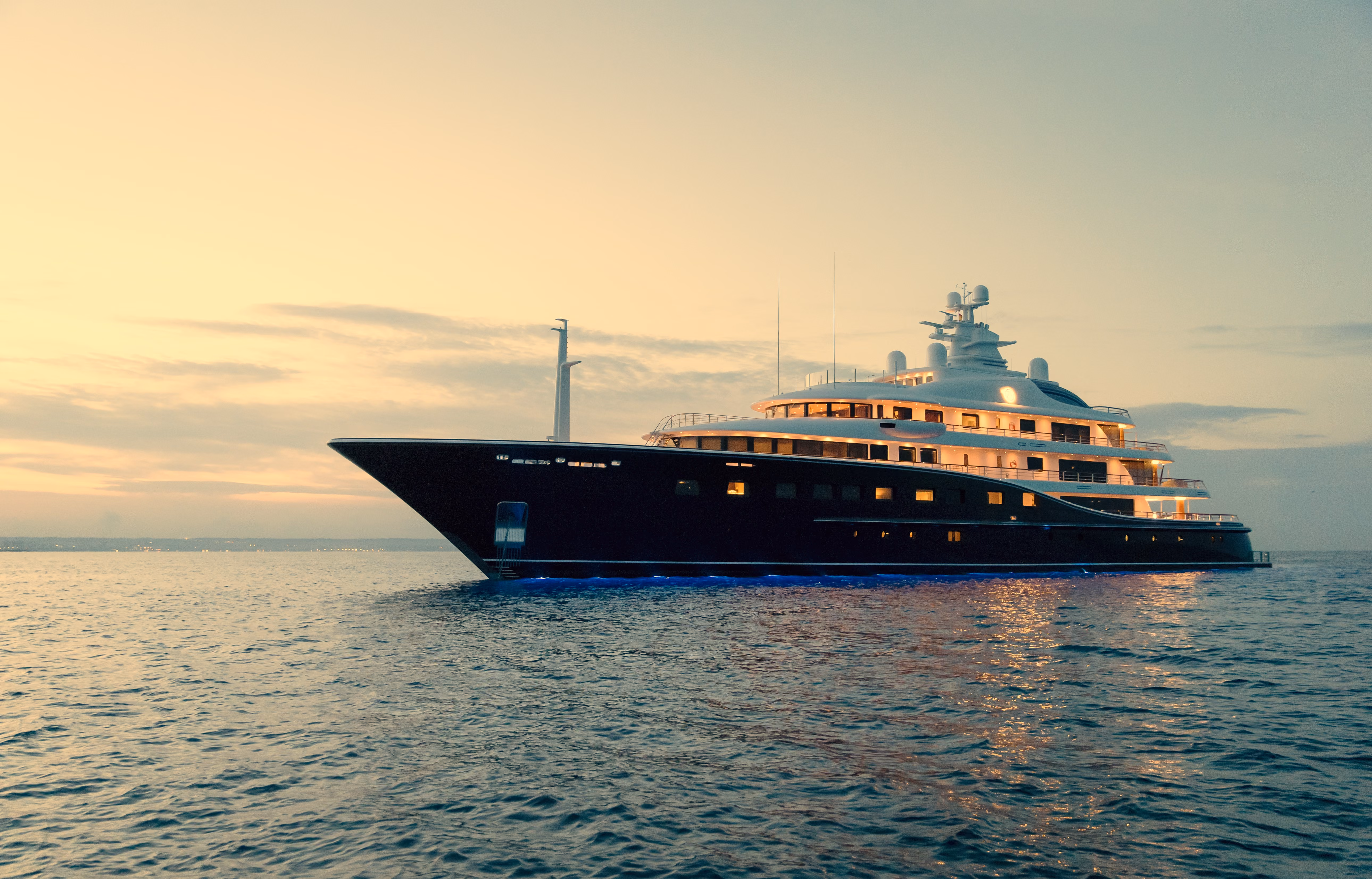 Luxusyacht bei Sonnenuntergang auf ruhigem Meer mit beleuchteten Kabinen.