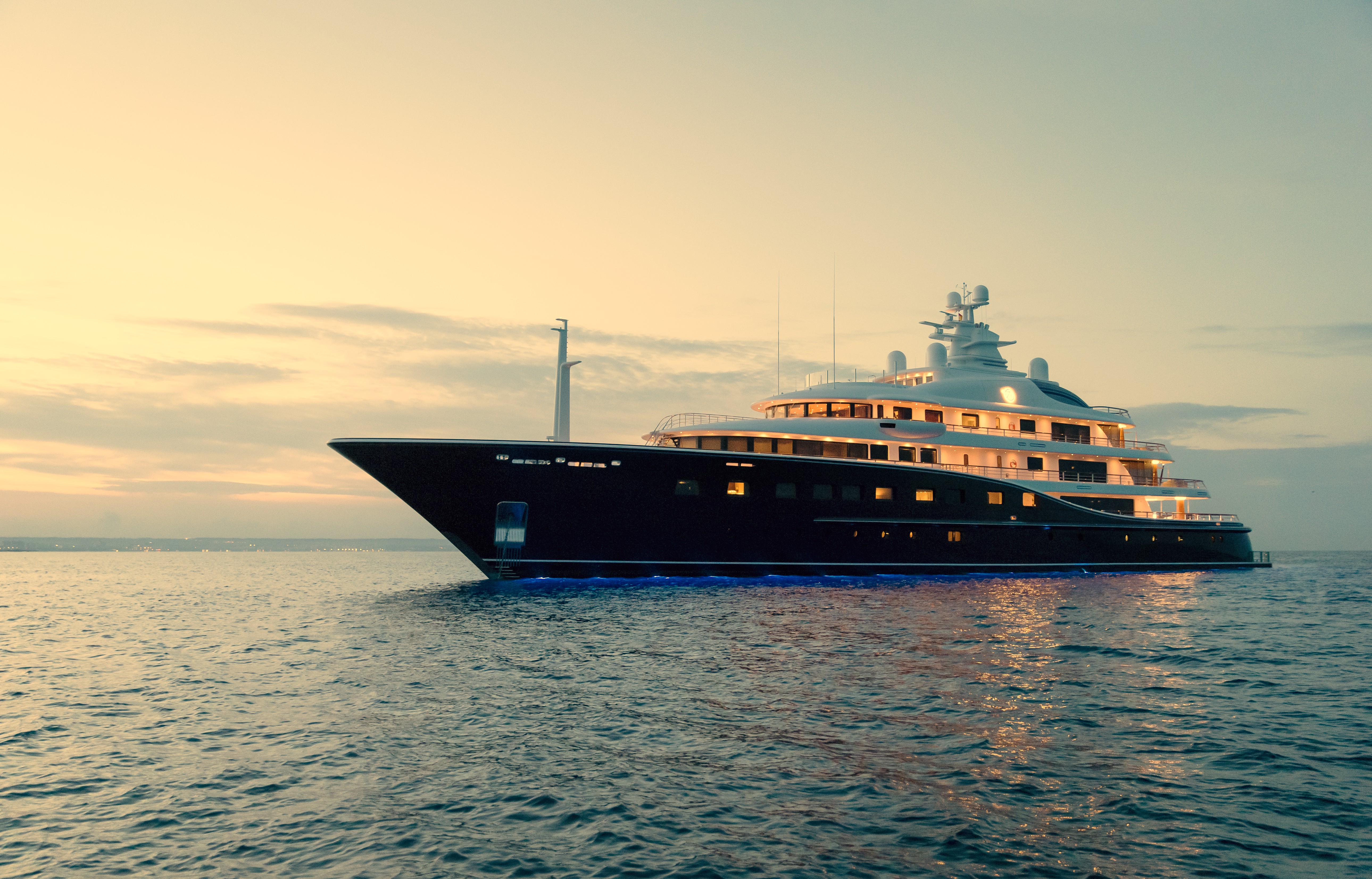 Luxusyacht bei Sonnenuntergang auf ruhigem Meer mit beleuchteten Kabinen.
