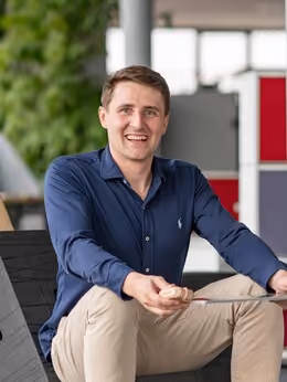 Mann lächelnd sitzt mit Tablet in der Hand in einem modernen Innenbereich.
