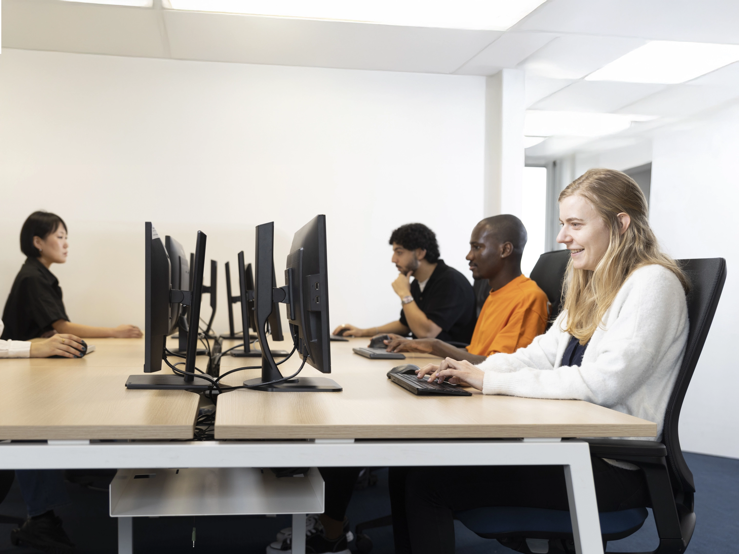 Quatre personnes de divers horizons travaillent sur des ordinateurs dans un bureau moderne et bien éclairé. ils passent une certification Pix 