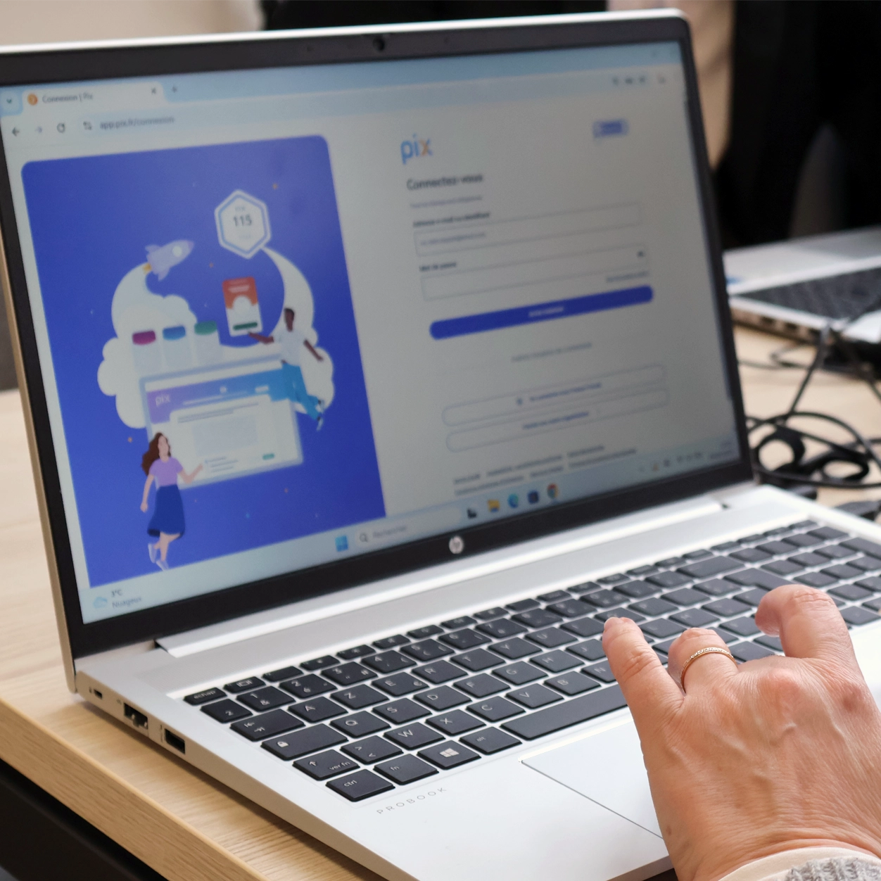 Une main utilise un ordinateur portable HP affichant une page de connexion au site Pix avec une illustration colorée à gauche.