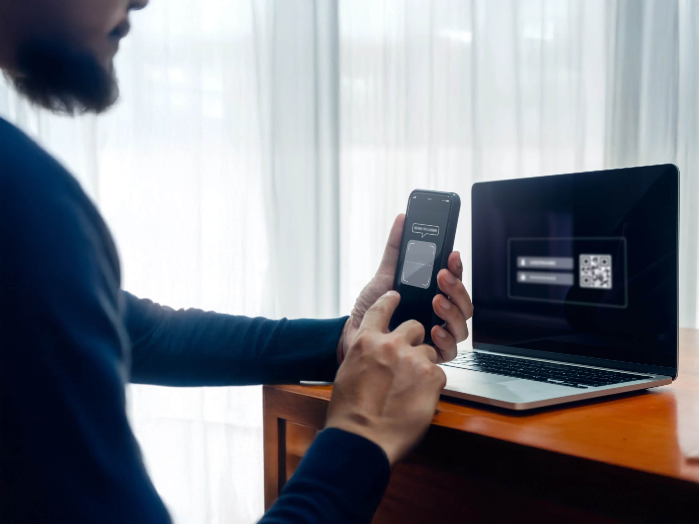 Un homme utilise son smartphone pour scanner un code QR à l'écran d'un ordinateur portable pour une connexion sécurisée.