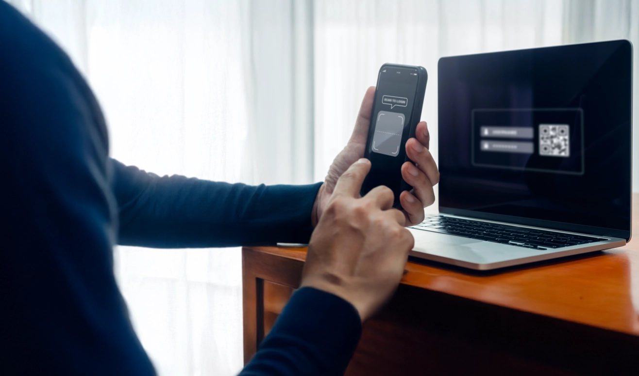 Une personne utilise un smartphone pour scanner un code QR affiché sur l'écran d'un ordinateur portable posé sur une table.