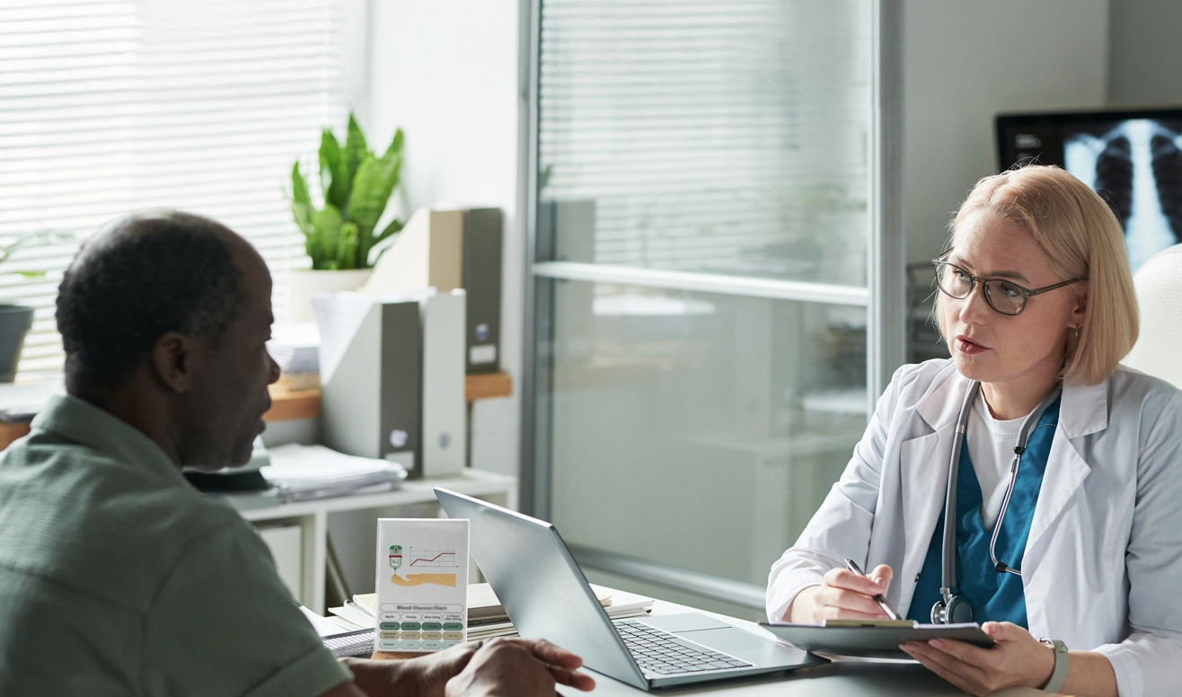 Médecin avec stéthoscope tenant un dossier et parlant avec un patient dans un bureau médical moderne avec ordinateur portable et radiographie.