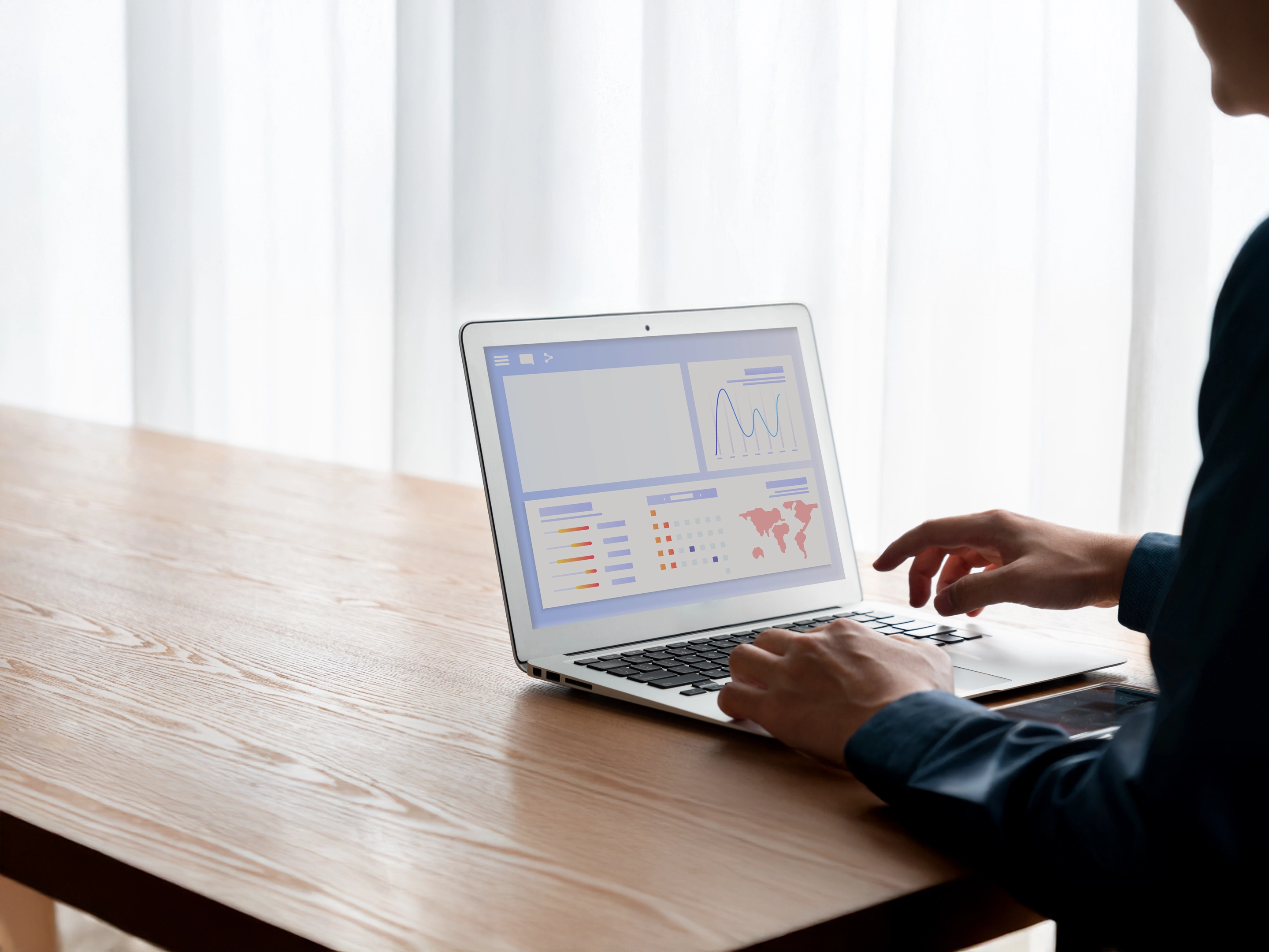 Person utilisant un ordinateur portable affichant des graphiques et des données analytiques sur une table en bois.