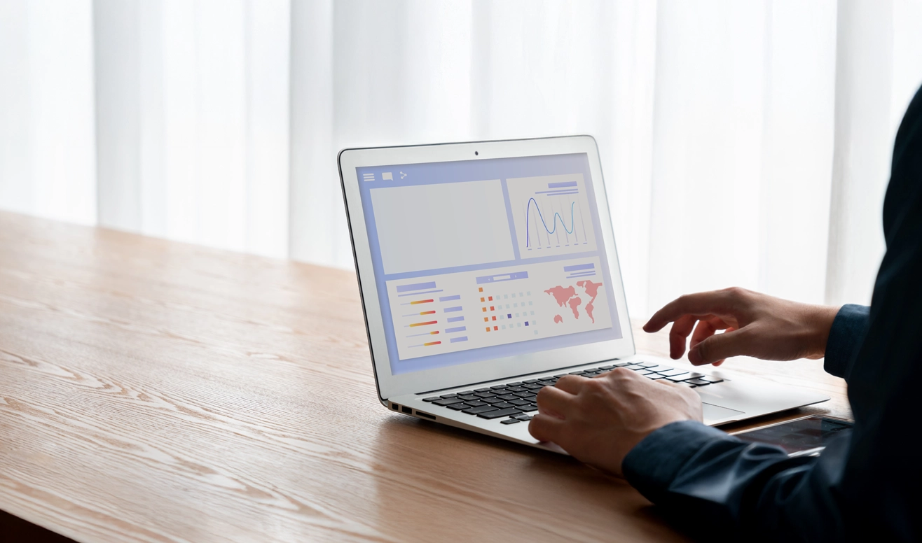 Person utilisant un ordinateur portable affichant des graphiques et une carte du monde sur un bureau en bois clair.