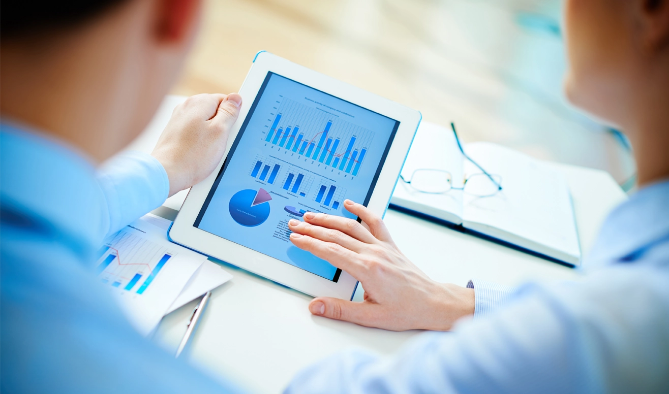 Deux personnes discutant devant une tablette affichant plusieurs graphiques et diagrammes en bleu.