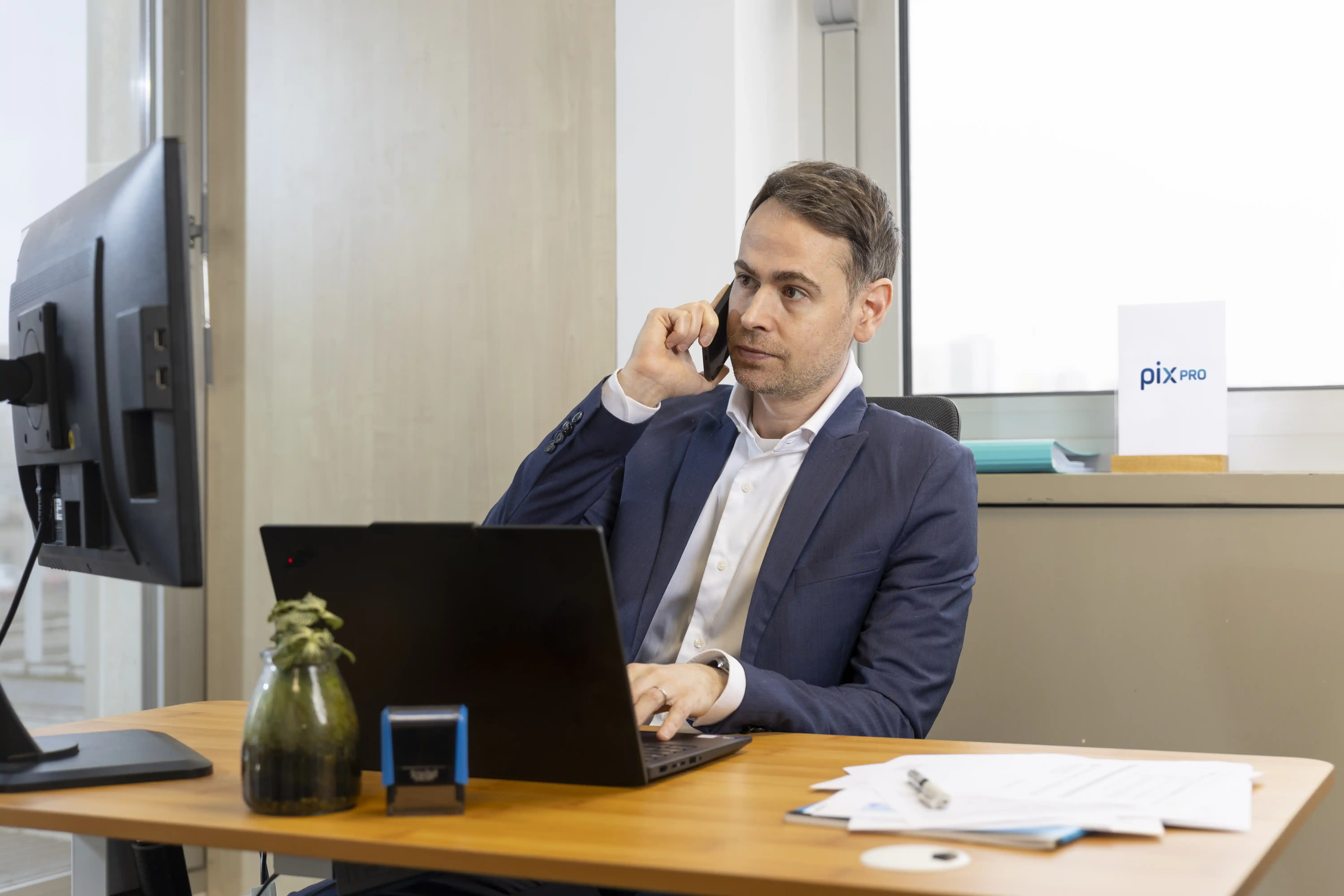 Homme d'affaires parlant au téléphone tout en travaillant sur un ordinateur portable à un bureau moderne.